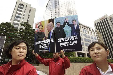 An activist holds up a banner showing photos of U.S. President Donald Trump, second from left, North Korean leader Kim Jong Un and South Korean President Moon Jae-in, right, during a rally wishing for peace on the Korea peninsular in front of Singapore Em