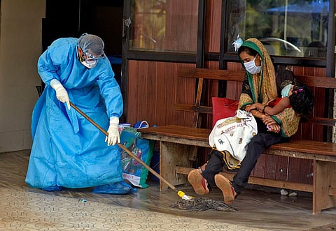 A staff of Medical College Hospital in Kozhikode wearing protective gear to safeguard from Nipah Virus fever, cleaning the floor with disinfectants without waking the child sleeping in the lap. (Express Photo)