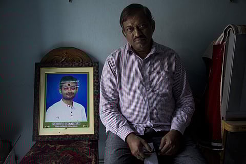 Koppu Ram Mohan, father of Indian student Sharath Koppu who was shot dead in the U.S. sits beside a photograph of his son in Hyderabad. (Photo | AP)