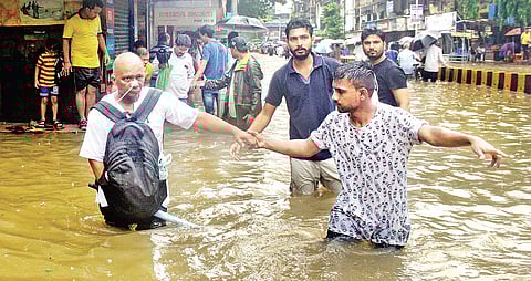 People walk along a flooded street during heavy showers in Mumbai. (File | EPS/Bhushan Loyande)
