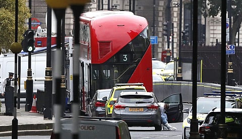 A forensics officers prepares to examine the scene near a car that crashed into security barriers outside the Houses of Parliament to the right of a bus in London, Tuesday, Aug. 14, 2018. | AP