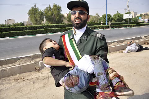 Iran's Revolutionary Guard member carries a wounded boy after a shooting during a military parade
