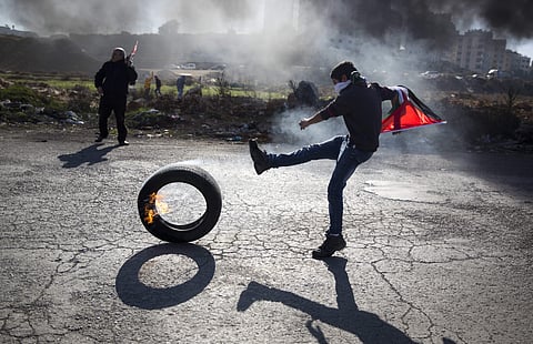 In this file photo, a Palestinian protester kicks a tire following protests against US. President Donald Trump's decision to recognize Jerusalem as the capital of Israel, in the West Bank city of Ramallah. (Photo |AP)