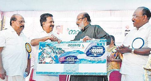 Finance Minister T M Thomas Isaac launches the Nava Kerala lottery by handing over a ticket replica to Opposition leader Ramesh Chennithala in Alappuzha on Monday | Express