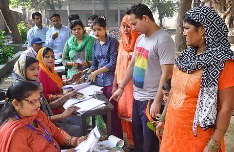 Polling officials conduct their procedure as voters wait to cast their votes at a polling station for the Haryana Assembly elections in Sonepat Monday. (Photo | PTI)