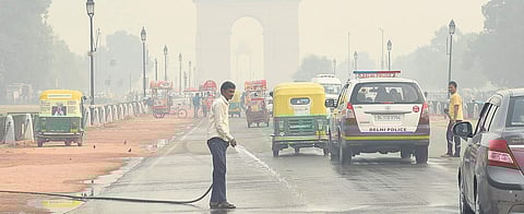 A worker sprays water on the road as vehicles move towards the India Gate, blanketed by thick smog in New Delhi. (Photo | Parveen Negi)