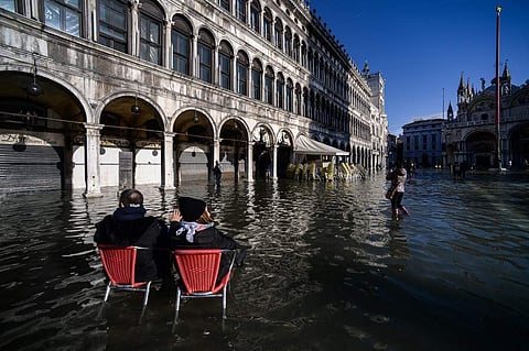 People sit on bistro chairs in the middle of the flooded St. Mark's Square on November 14, 2019 in Venice. (Photo | AFP)