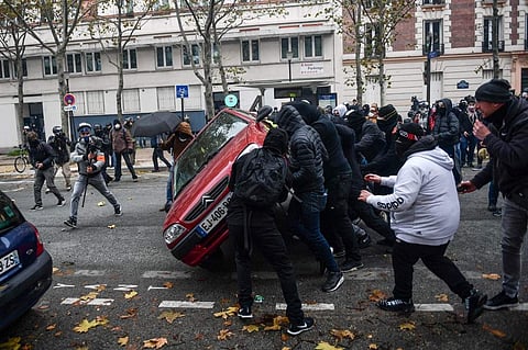 Persons wearing black hoodies lift a car near place d'Italie in Paris on November 16, 2019, during a demonstration of the 'yellow vest' (gilets jaunes) marking the first anniversary of the movement. (Photo | AFP)
