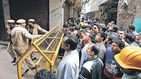 Locals gather behind a police barricade to watch a MCD inspection at the building that caught fire on Sunday, in Anaj Mandi area on Wednesday (Photo | Arun Kumar, EPS)