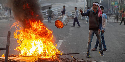 A protester throws a tin onto a fire made to block traffic in Gauhati. (Photo | AP)