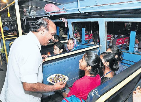 Revenue Minister E Chandrasekharan offers sweets to students who reached Kasaragod bus stand from Mangaluru on Saturday evening. District Collector D Sajith Babu had deployed five special buses to bring the students home | EXPRESS