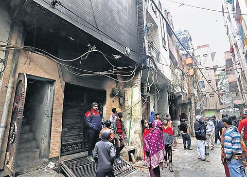Locals stand outside the building in Krishna Nagar which was engulfed in flames in the wee hours of Thursday. (Photo | EPS)