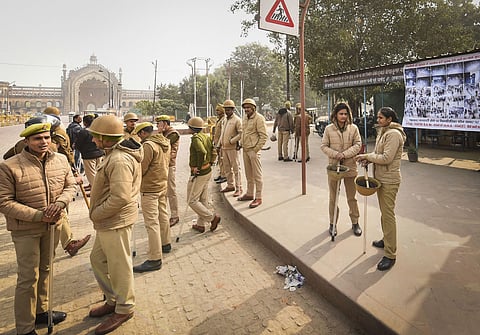 Police personnel stand guard beside a poster of protestors suspected to have incited vandalism during protests against CAA and NRC in Lucknow Friday. (Photo | PTI)