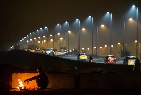 A man warms himself by a bonfire as cars ply in the background on a cold and wintry night in New Delhi. (Photo | PTI)