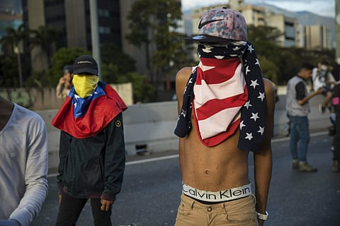 An anti-government protester using a US flag as a mask returning from a demonstration in Caracas, Venezuela (Photo | AP)