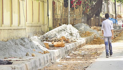With construction material dumped on a footpath near Kumble Circle, people are forced to walk on the road. (Photo | Pandarinath B, EPS)