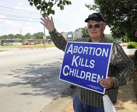 A man waves to passing cars while holding an anti-abortion sign in front of the Alabama Women's Wellness Center in Huntsville (Photo| AP)