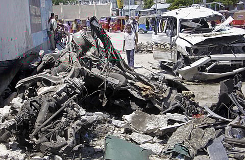 Somalis walk near the wreckage after a suicide car bomb attack in Mogadishu (Photo | AP)
