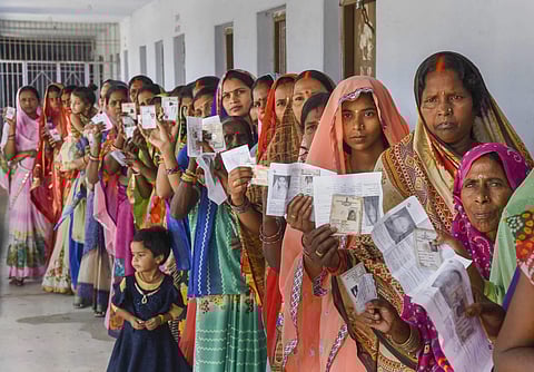 Women show their voter identity cards as they stand in a queue at a polling station. (Photo | PTI)