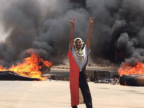 A protester flashes the victory sign in front of burning tires and debris on road 60, near Khartoum's army headquarters, in Khartoum, Sudan (photo | AP)