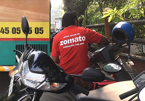 A delivery man working with the food delivery app Zomato sits on his bike in a business district in Mumbai (File photo | AFP)