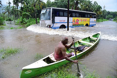 Road flooded due to overflowing Pooyamkutty river and an old man manoeuvering his boat through the road when a KSRTC bus passes near it at Nyayapalli near Kuttumpuzha on Thursday. (Photo | Albin Mathew, EPS)