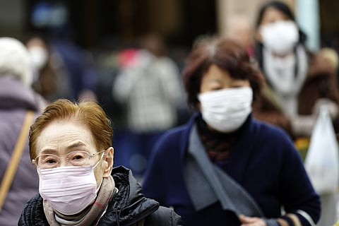 Pedestrians wear protective masks as they walk through a shopping district in Tokyo. (Photo | AP)