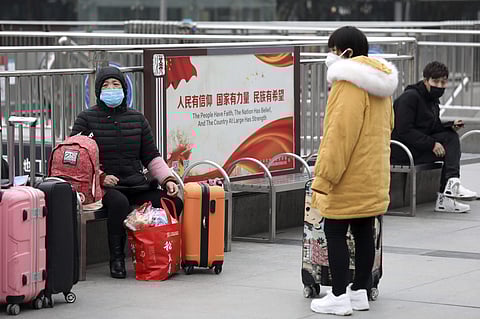 Travellers sit with their luggage outside the closed Hankou Railway Station in Wuhan in central China's Hubei Province. (Photo| AP)