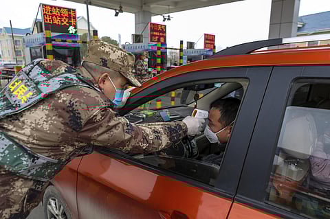 A militia member uses a digital thermometer to take a driver's temperature at a checkpoint at a highway toll gate in Wuhan in central China's Hubei Province. (Photo| AP)