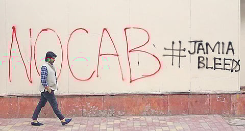 A man passes by a wall with graffiti about the recently amended Citizenship Act, outside Jamia Millia Islamia (File Photo | Arun Kumar, EPS)