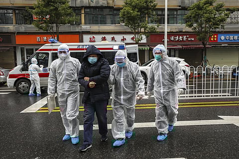 Medical workers in protective gear help a patient near an ambulance in Wuhan. (Photo | AP)