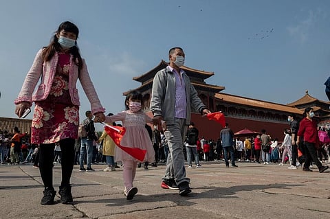 A family wearing face masks as a preventive measure against the Covid-19 coronavirus walk outside the Forbidden City during holiday. (Photo| AFP)