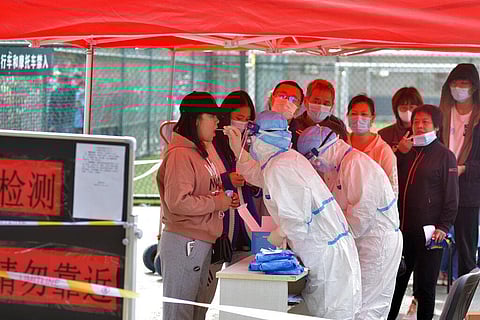 A medical staff takes a swab from a woman as residents line up for the COVID-19 test near the residential area in Qingdao in east China's Shandong province. (Photo | AP)