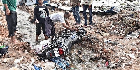 A resident of Baba Nagar in Hyderabad cleans his sludge-ridden motorcycle five days after the floods, as others look on. (Photo| Vinay Madapu, EPS)