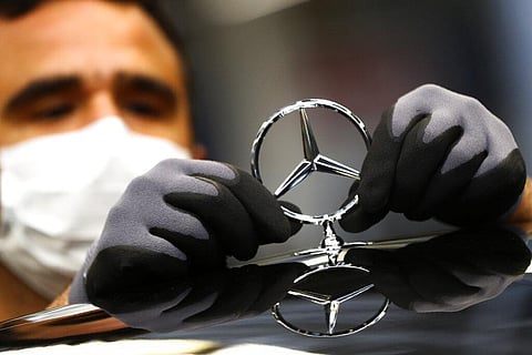 An employee attaches a Mercedes emblem as he works on a Mercedes-Benz S-class car at the Mercedes plant in Germany. (Photo | AP)