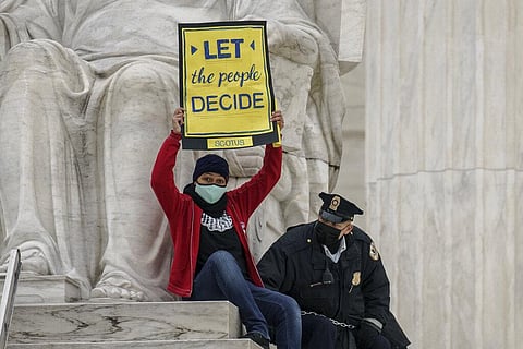 A protester opposed to the Senate's race to confirm Amy Coney Barrett is removed by police after chaining themselves to a railing and holding a sign while sitting atop a statue, at US Supreme Court. (