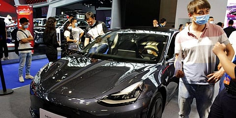 Visitors wearing face masks look at a Tesla Model 3 vehicle on display at an auto show in southwestern China. (File photo| AP)