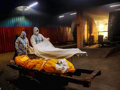 A relative along with a health worker helps to place the body of a person who died from COVID-19 before cremation. (File Photo| PTI)