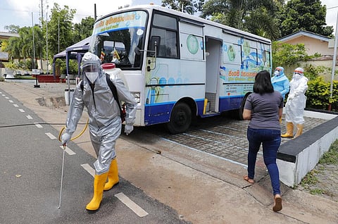 A Sri Lankan health worker sprays disinfectants as people wait to give swab samples to test for COVID-19 near a mobile testing vehicle outside a hospital in Minuwangoda, Sri Lanka. (Photo | AP)