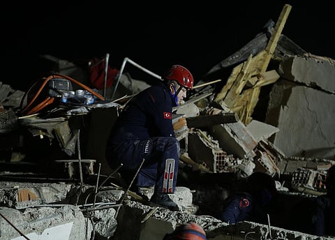 A member of rescue services, kneels to listen during the ongoing search for survivors in the debris of a collapsed building in Izmir, Turkey. (Photo | AP)