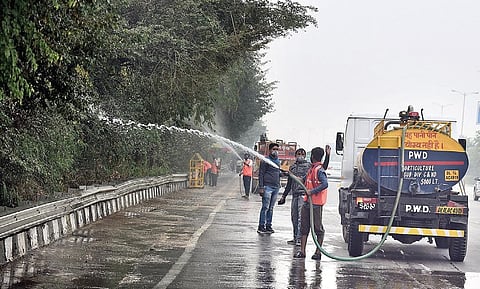 PWD workers spray water on trees to reduce dust near Raj Ghat Bus Depot during the vist of AAP’s Gopal Rai. (Photo | Parveen Negi, EPS)