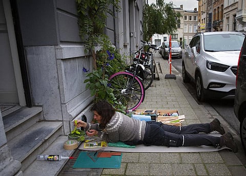 Belgian artist Elke Lemmens lays on the sidewalk as she installs a miniature scene into a boot scraper in Antwerp, Belgium. (Photo | AP)