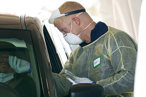 A worker wearing gloves, a face shield, a mask, and other PPE administers a COVID-19 test at a King County coronavirus testing site in Auburn, Wash., south of Seattle. (Photo | AP)