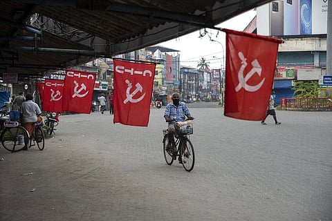 A man wearing mask as a precaution against COVID-19 pedals past flags of a Communist party trade union during a nation wide strike by various trade unions in Kochi. (Photo | AP)
