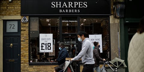 People walk past as barber Matthew Jones stands inside his temporarily closed 'Sharpes Barbers' on Broadway Market in east London's Hackney. (Photo| AP)