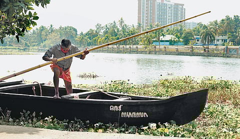 Shanmughan rowing his country boat in the backwaters near the site of the demolished highrises.