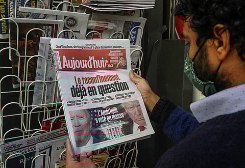 A man wearing a face mask as a precaution against the coronavirus reads the headlines about the U.S. presidential elections at a newspapers stand in Paris. (Photo | AP)