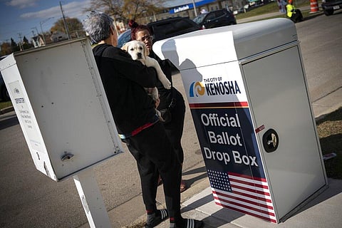 A woman carries her puppy as she drops off her ballot at Kenosha's municipal offices for early voting in Kenosha. (Photo | AP)