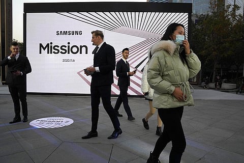 A woman wearing a mask to protect herself from the coronavirus walks pass foreign models taking part in a promotion event in Beijing on Friday, Nov. 6, 2020. (Photo | AP)