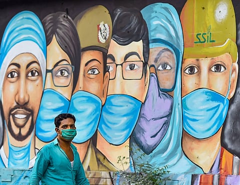 A man walks past a mural made in honour of COVID-19 warriors. (File Photo| PTI)